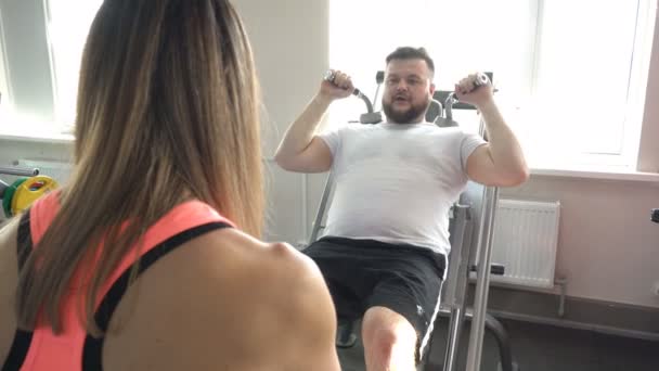 Bir sakallı bir beyaz adam egzersizleri bir uyluk, bacak kasları için yeni bir spor salonunda kişisel bir eğitmen ile gerçekleştirir — Stok video