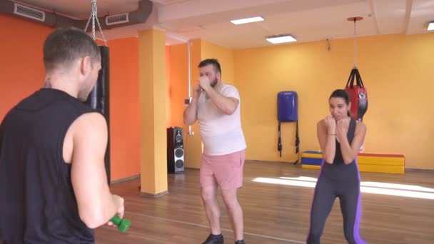 Un entraîneur masculin caucasien enseigne à un homme et une fille barbus le bon coup de poing dans l'art martial, l'auto-défense, la gym, le ralenti — Video