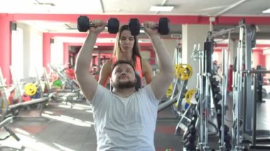 Bir sakallı bir beyaz adam bir güzel kız eğitmen yardımı ile oturan spor salonu bench halter bir egzersiz yapar