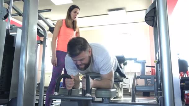 Een blanke man met een baard is betrokken bij de sportschool met een persoonlijke trainer op een been spier uitoefenaar, buigen van de benen in de knieën, fitness — Stockvideo