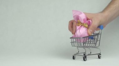 El bırakır bir pembe hediye Easter egg arka planda bir alışveriş sepeti beyaz kopya alanı, kavram süpermarket mans