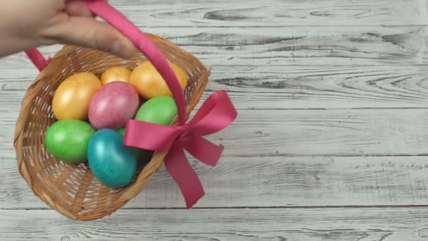 Mano masculina pone una cesta de regalo con huevos de pollo de colores sobre un fondo blanco de madera, vacaciones de Pascua, espacio para copiar, celebración — Vídeos de Stock