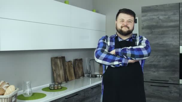 Bir aşçı giyen önlük olarak kalın sakallı adam modern bir mutfak ve kameraya doğru görünüyor — Stok video