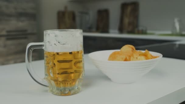 A glass pint mug of pilsener or lager beer with potato chips are in the kitchen — Stock Video