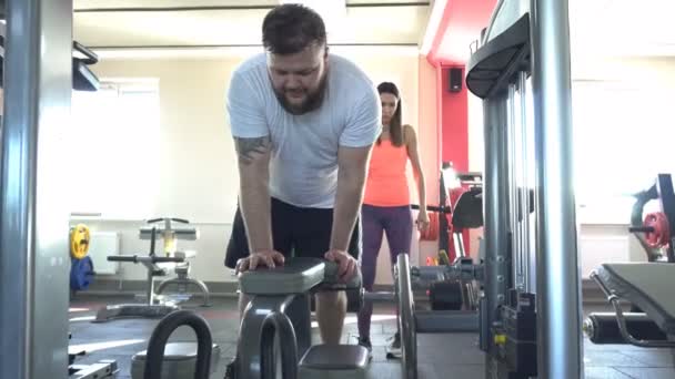 Un hombre caucásico con barba se dedica al gimnasio con un entrenador individual en un ejercitador muscular de la pierna, doblando las piernas en las rodillas — Vídeos de Stock