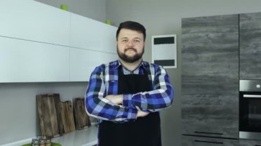 Bir önlük giyen bir aşçı olarak sakallı şişman beyaz erkek bir mutfak ve kameraya doğru görünüyor