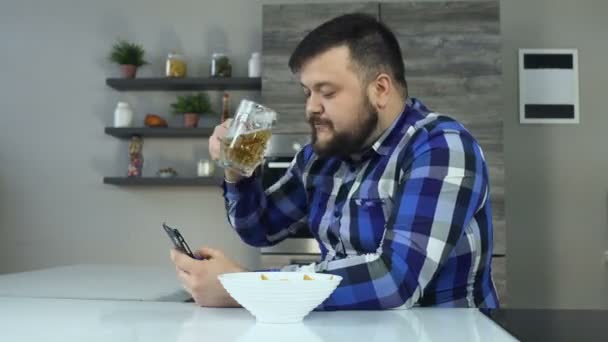 Timelapse fat bearded man drinks beer, eats chips and looks news feed in smartphone. Thick guy surfs in internet and chatting with followers or subscribers in social networking service — Stock Video