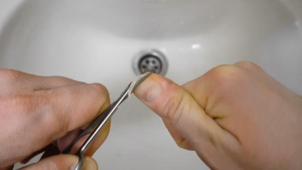 Macho se corta la uña por tijeras sobre un lavabo o un lavabo por la mañana — Vídeo de stock