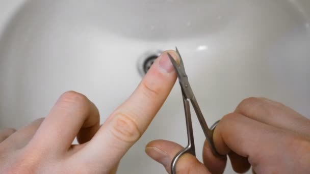 El hombre se corta la uña con tijeras sobre un lavabo o un lavabo por la mañana. — Vídeo de stock