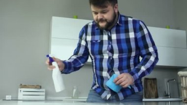 süngerimsi bez peçete ve sprey ile gömlek giyen kalın sakallı adam kir, yağ ve lekeleri kirli yüzeyde modern mutfak temizler