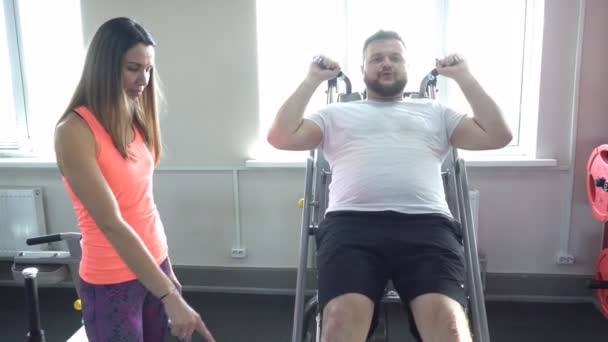 Nice girl trainer explique à un homme caucasien la justesse de faire un exercice pour les muscles des jambes sur un simulateur hackenshmidt, un gymnase moderne — Video