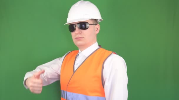 Jefe masculino en gafas negras en un objeto de construcción muestra un gesto todo está bien, un pulgar hacia arriba, fondo verde, hromakey, espacio de copia, ingeniería de seguridad — Vídeo de stock