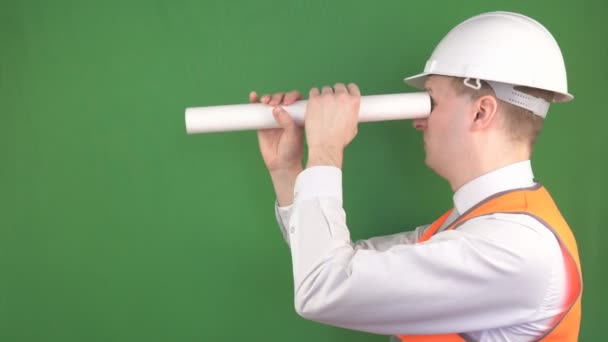 Un ingeniero joven frívolo y divertido mira en el dibujo como un tubo, juega al tonto, se burla, fondo, cromakey, fabricación — Vídeos de Stock