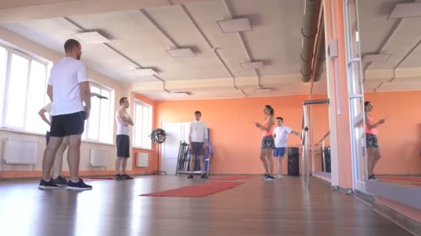 Vacker kaukasiska flicka tränare i gymmet förklarar för killarna i gymmet riktigheten av övningarna i paret gruppträning — Stockvideo