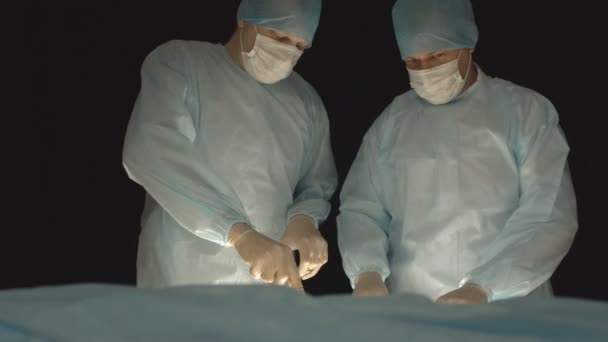 Twee mannelijke chirurgen voeren een chirurgische operatie uit. Zwarte achtergrond, gezondheidszorg, moderne technologieën — Stockvideo