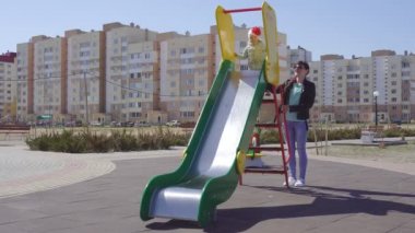Beyaz anne ve onun eğlenceli küçük kızı renkli, yeni ve modern bir oyun alanında oynarken, bir tepeden aşağı binmek
