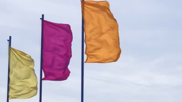 Drapeaux de fête multicolores jaune orangé et rouge flottant dans le vent sur un fond bleu ciel, espace de copie — Video