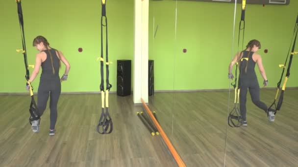 Девочка выполняет упражнения TRX hinge в современном тренажерном зале, силовые тренировки — стоковое видео