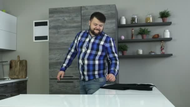 En la cocina el hombre alegre gordo con la barba se pone el delantal. Chico regordete camina con una marcha de baile . — Vídeos de Stock