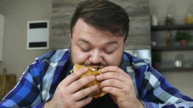 Sakallı dolgun adam bir parça hamburger ısırır. Yemekler çok lezzetli. Tombul adam memnun. Sağlıksız Yaşam Tarzı, kızarmış ve yüksek kalorili gıda. Obezite ve aşırı kiloluluk riski. Yavaş çekim
