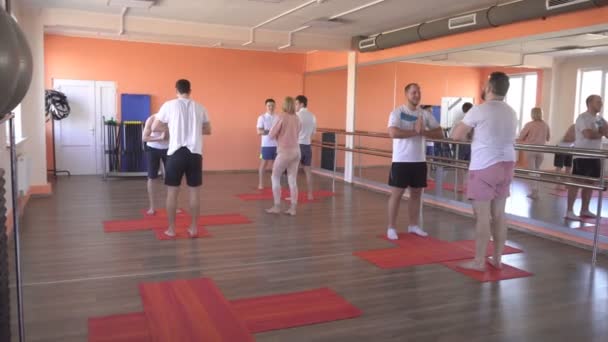 Vacker kaukasiska kvinnlig instruktör undervisar Yoga tekniker i en manlig grupp session. stärka muskler och hälsa med asanas i yoga, modernt gym — Stockvideo