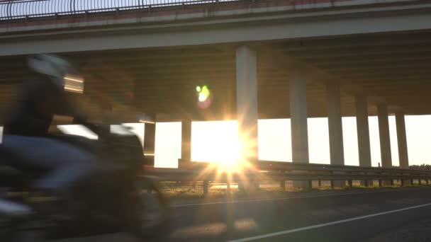 Motociclista monta en una motocicleta en el fondo de un puente de carretera y una puesta de sol. Concepto de viaje y motocicleta, espacio para copiar — Vídeo de stock