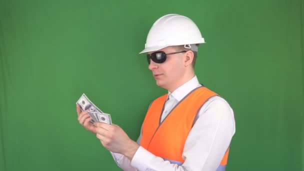 O chefe em um capacete de construção e um colete de sinal relata dólares de dinheiro depois de uma transação bem sucedida, fundo verde, hromakey, supervisor — Vídeo de Stock