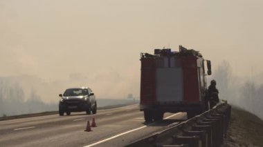 Yolda bir itfaiye civarı ile itfaiye aracı bir orman yangını söndürür, yoğun duman, tehlike