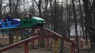 İnsanlar Bobruisk, Beyaz Rusya 03.09.19 baharda parkta bir şehir fuarında bir rollercoaster binmek. Erkekler ve çocuklar ellerini sallıyor. Cazibe demiryolu üzerinde hızlı gider.