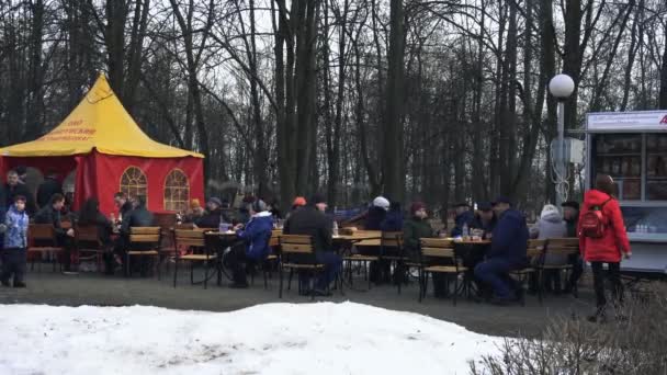 İnsanlar şehir parkında masalarda oturup Bobruisk, Belarus 03.09.19 tatil Maslenitsa sırasında yemek. Vatandaşlar lunaparkta masalarda ve şenlikler sırasında yemek yiyor. — Stok video