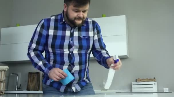 Plump guy cleans soiled kitchen with a duster, bleach, cleaning product. Carefully wipes the table. Timelapse video Fat man in jeans and shirt with spongy cloth napkin and spray cleans surface from — Stock Video