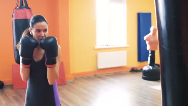 Una donna con i guanti da boxe batte il sacco da boxe in palestra con l'allenatore personale. Allenati con l'istruttore in un fitness club. Esercitazioni individuali di perdita di peso per ragazza. Addestratore privato per donne. Fare esercizi — Video Stock