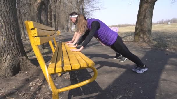 Przyjaciele młoda dziewczyna i człowiek grać sportu wiosną na naturę w parku, push-upy z ławce, trening siłowy, powolny mo — Wideo stockowe