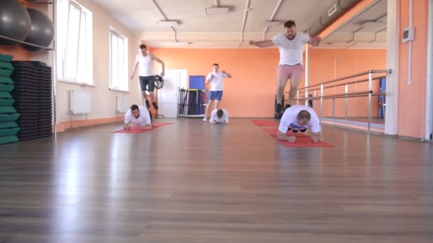 Caucásico amigos masculinos se dedican a la aptitud en el gimnasio, realizar saltos de par. Clases de fitness en grupo, cámara lenta — Vídeo de stock