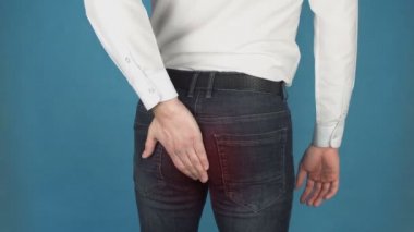 Adam hemoroid nedeniyle ağrı vardır. Bilgisayarda uzun süreli çalışma nedeniyle anal kanalda kazık veya hemoroidal hastalık kavramı. Beyaz gömlekli adam eliyle kalçasına dokunur. Kırmızı nokta olarak