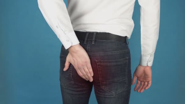 Man has pain due to Hemorrhoids. Concept of piles or hemorrhoidal disease in in the anal canal due to long-term work at the computer. Man in white shirt touches his buttocks with his hand. Red spot as — Stock Video
