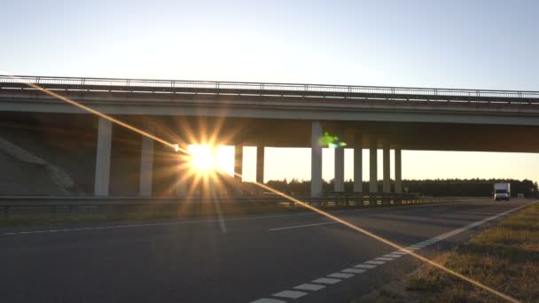 Солнечный закат на фоне шоссе с мостом, через который перевозится фура с продовольствием — стоковое видео