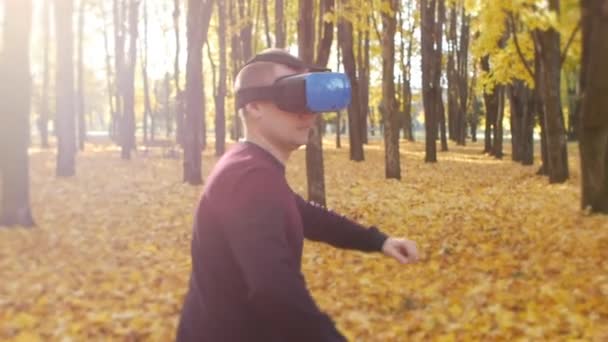 Ο τύπος με τα ακουστικά εικονικής πραγματικότητας τρέχει στο φθινοπωρινό πάρκο, ο άνθρωπος στην οθόνη που τοποθετείται στο κεφάλι. Φανατικός παίκτης. Το φύλλο πέφτει σε μια πόλη την ηλιόλουστη μέρα. Όμορφη φύση — Αρχείο Βίντεο