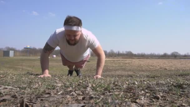 Strong caucasian man with a beard playing sports in nature performs pushups in the sand, slow motion, activity — Stock Video