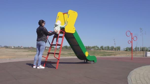 Кавказская мать и ее игривая маленькая дочь играют на красочной, новой и современной детской площадке, скачут с холма, счастье — стоковое видео