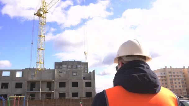 Hombre maestro en un chaleco de señal y un casco supervisa la construcción de una casa de panel residencial, espacio de copia — Vídeo de stock