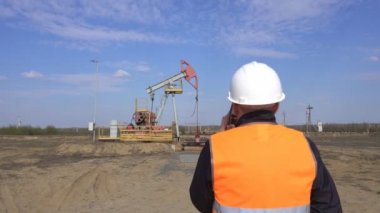 Bir sinyal yelek erkek baş müfettiş bir pompa istasyonu petrol, gaz ve yanıcı yakıt endüstrisi, pumpjack, mühendislik arka planda telefonda konuşurken