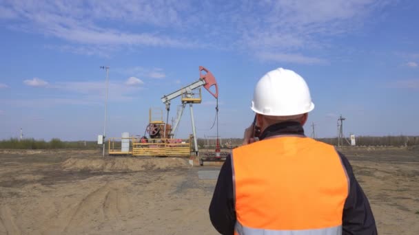 Manlig Chief Inspector i en signalväst talar i telefon på bakgrunden av en pumpstation olja, gas och brännbar bränsle industri, Pumpjack, Engineering — Stockvideo