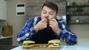 Tombul adam hamburgerini seviyor. Ketçapın erkek parmakları bitiyor. Sakallı şişman adam bir parça hamburger ısırır. Yemekler çok lezzetli. Sağlıksız Yaşam Tarzı. Obezite riski ve