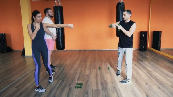 Instructor privado explica a un hombre gordo, chica delgada en el gimnasio. Entrenamiento con pesas. Taladros individuales de pérdida de peso para tipo grueso. Entrenamiento con entrenador personal en un pabellón deportivo. Hacer ejercicios y — Vídeo de stock