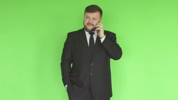 Een blanke man in een zwart Business Suit met een baard lost problemen telefonisch op op de achtergrond van een groene muur, het beheren van — Stockvideo