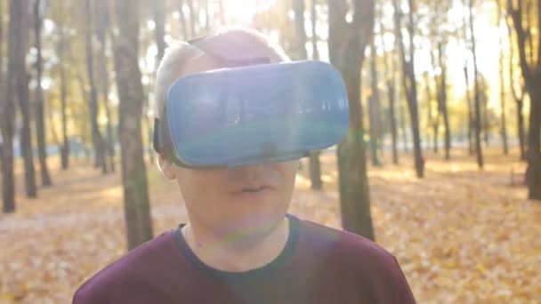 Man in vr-headset raakt door zijn handen Virtual Reality, Guy in head-mounted display in het herfst Park op zonnige dag — Stockvideo