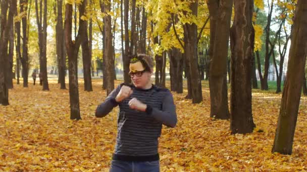 卷曲的有趣和快乐的男人在秋天的公园里跳舞,滑稽和欢快的人类情感。在阳光明媚的日子里,树叶落在一个小镇上。美丽的自然风光 — 图库视频影像