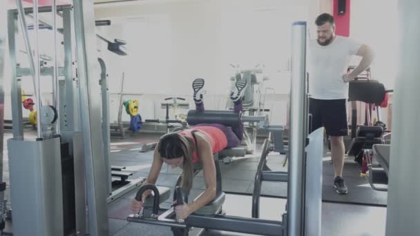 Prywatne kobiety trener pokazuje człowieka, jak zrobić ćwiczenia na symulatorze w siłowni. Facet zamierza huśtawka mięśnie nóg z indywidualnym instruktorem. Ćwiczenia odchudzania z osobistego trenera w klubie fitness — Wideo stockowe