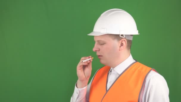 Un hombre caucásico en un chaleco de señal y un casco protector quiere fumar un cigarrillo en el lugar de trabajo, un concepto de seguridad en el lugar de trabajo y los incendios, hromakey — Vídeo de stock